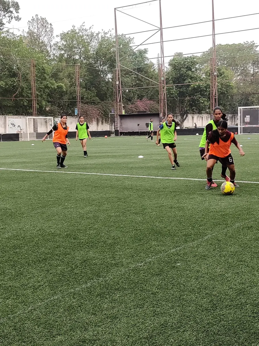 Women in bibs playing a small-sided training match on a turf pitch at a She Kicks academy session