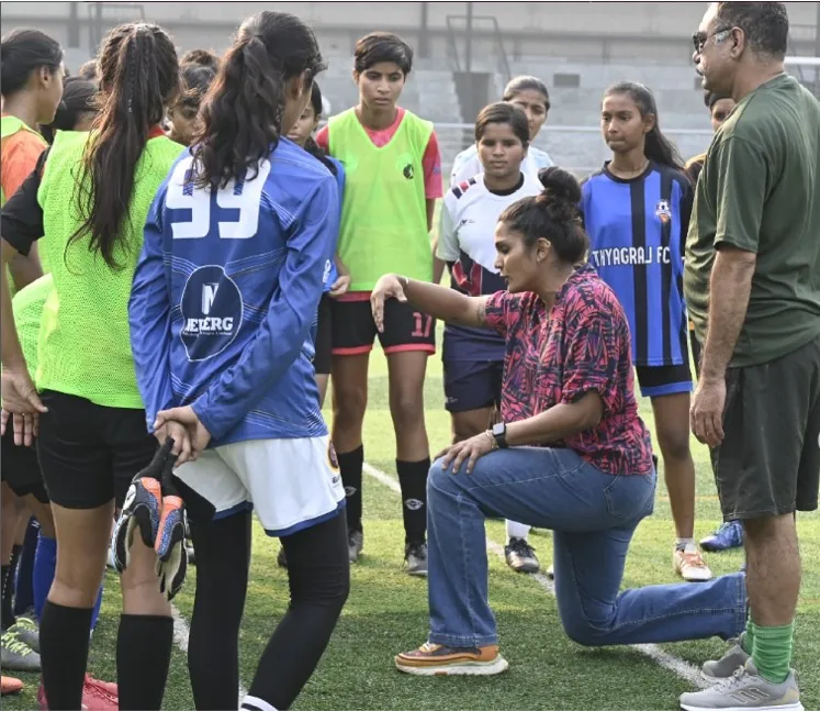 Aditi Chauhan kneeling to brief a huddle of girls in bibs during a training session