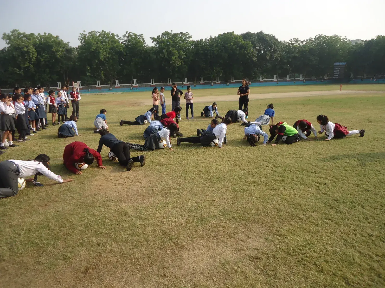 Schoolgirls in uniform doing ball-control drills on a school ground as a coach supervises