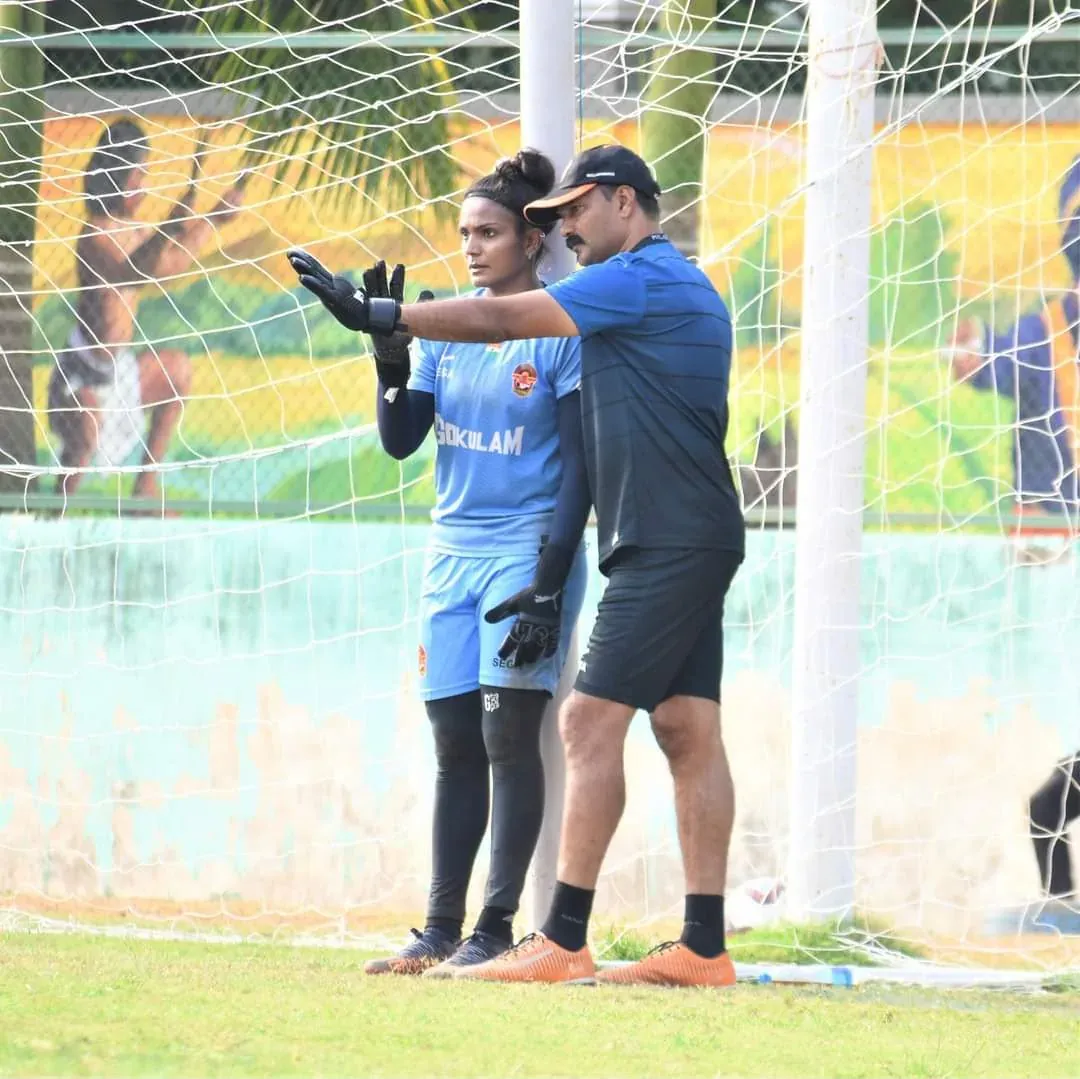 A goalkeeper in a Gokulam Kerala kit training one-on-one with a goalkeeping coach by the goal.