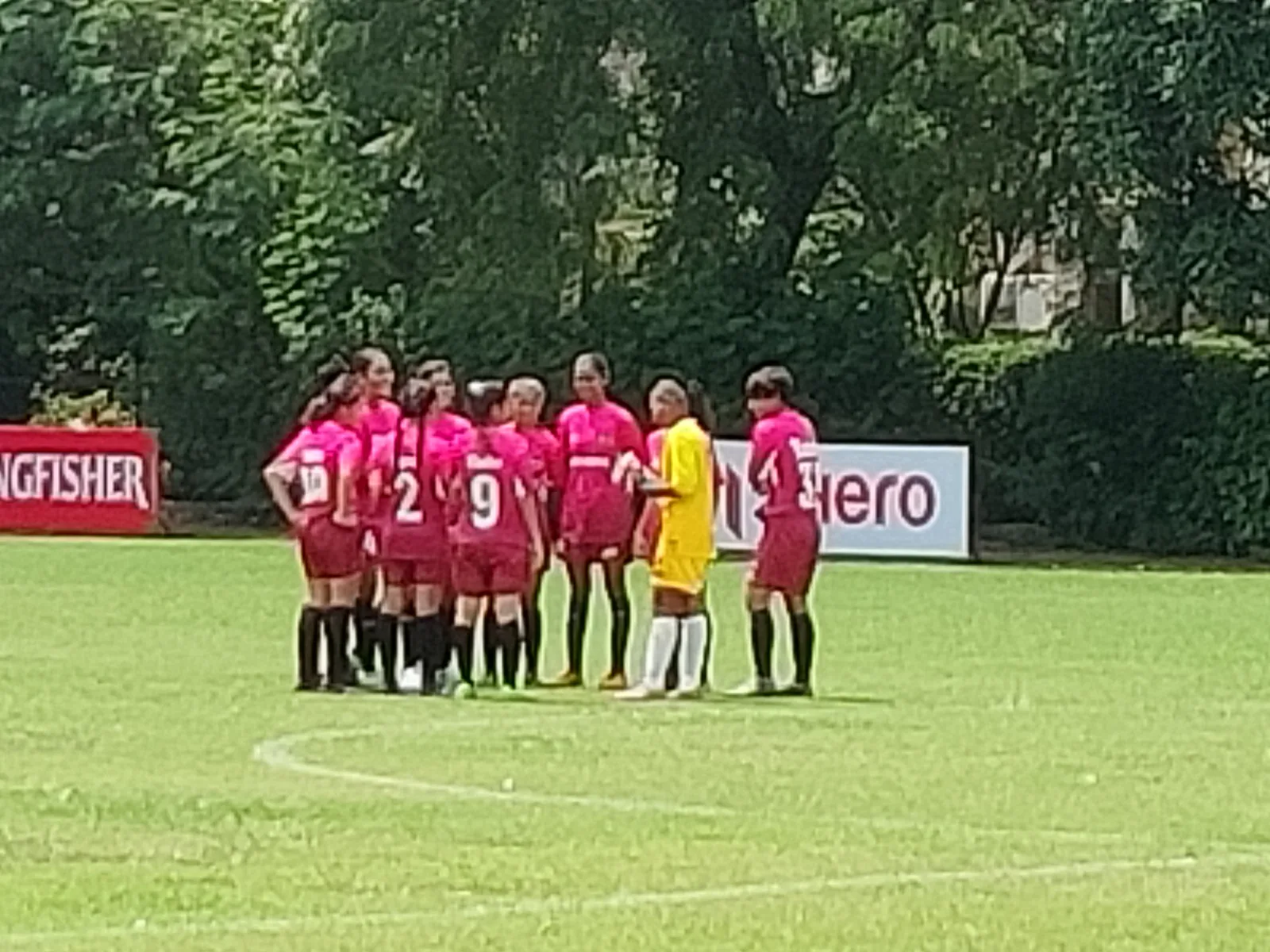 A She Kicks girls' team in a pre-match huddle in pink kit before a match