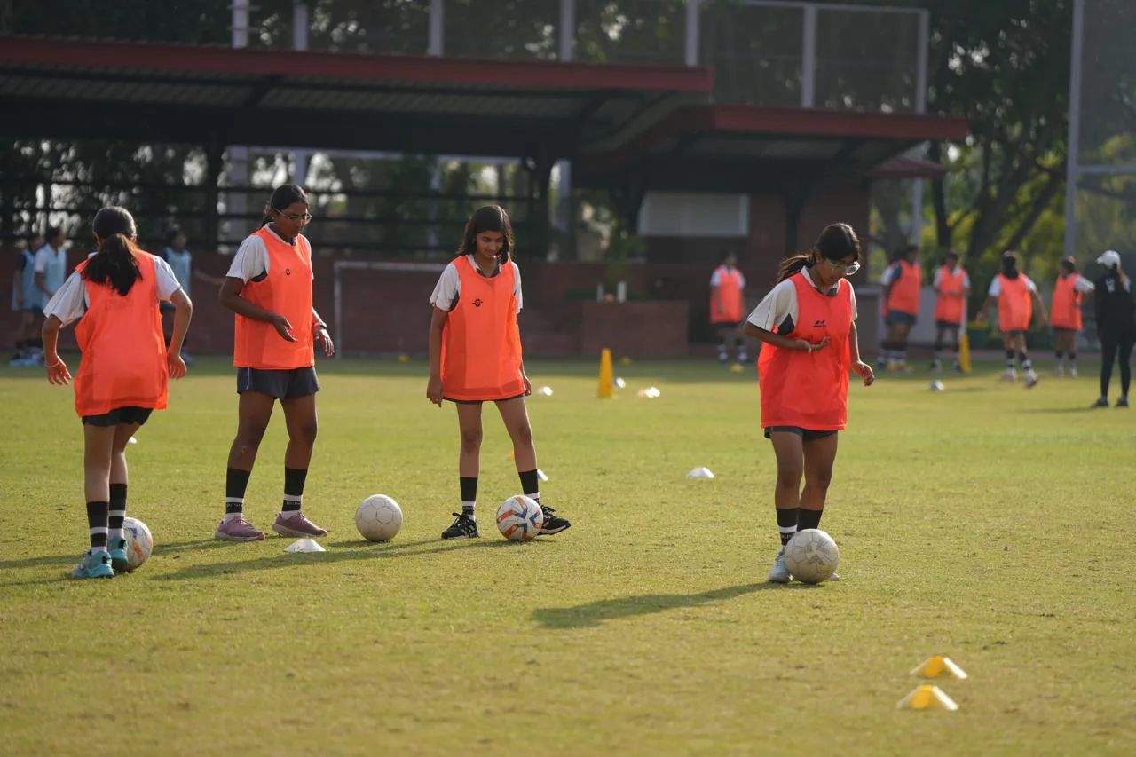 Girls in orange bibs practising a dribbling drill on a training pitch