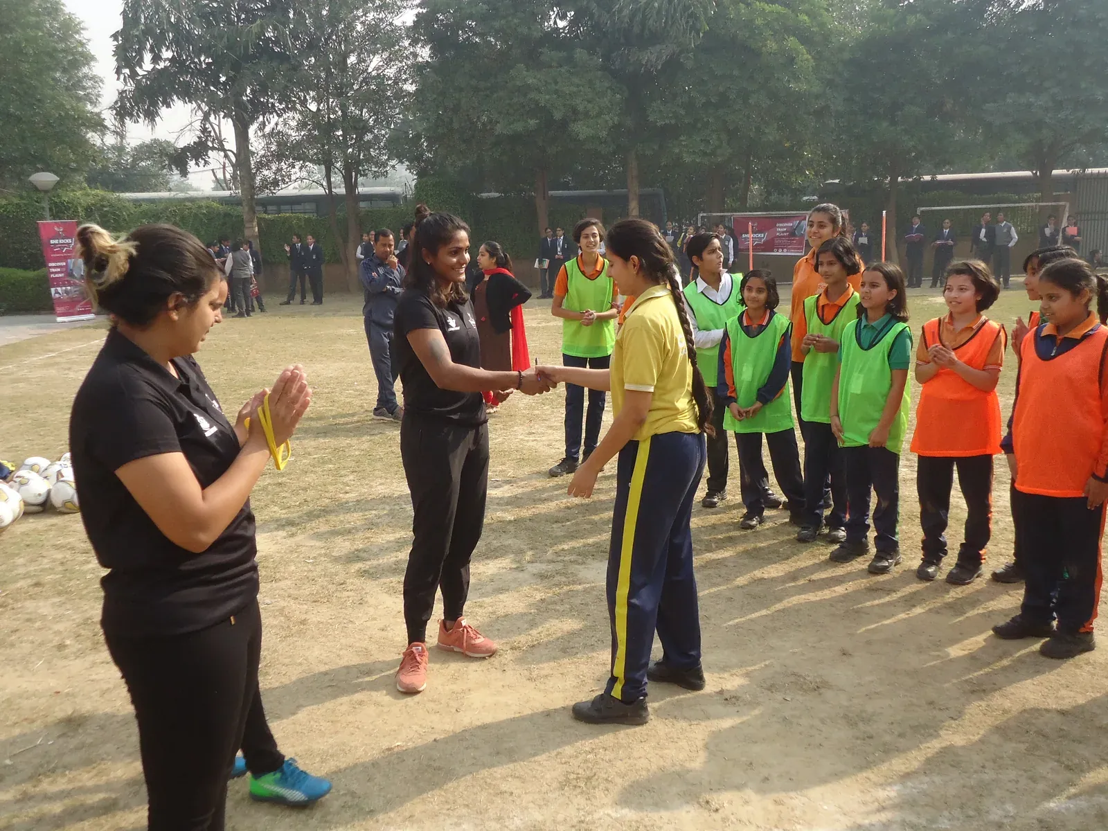 Aditi Chauhan shaking hands with a schoolgirl as girls in bibs applaud at a session