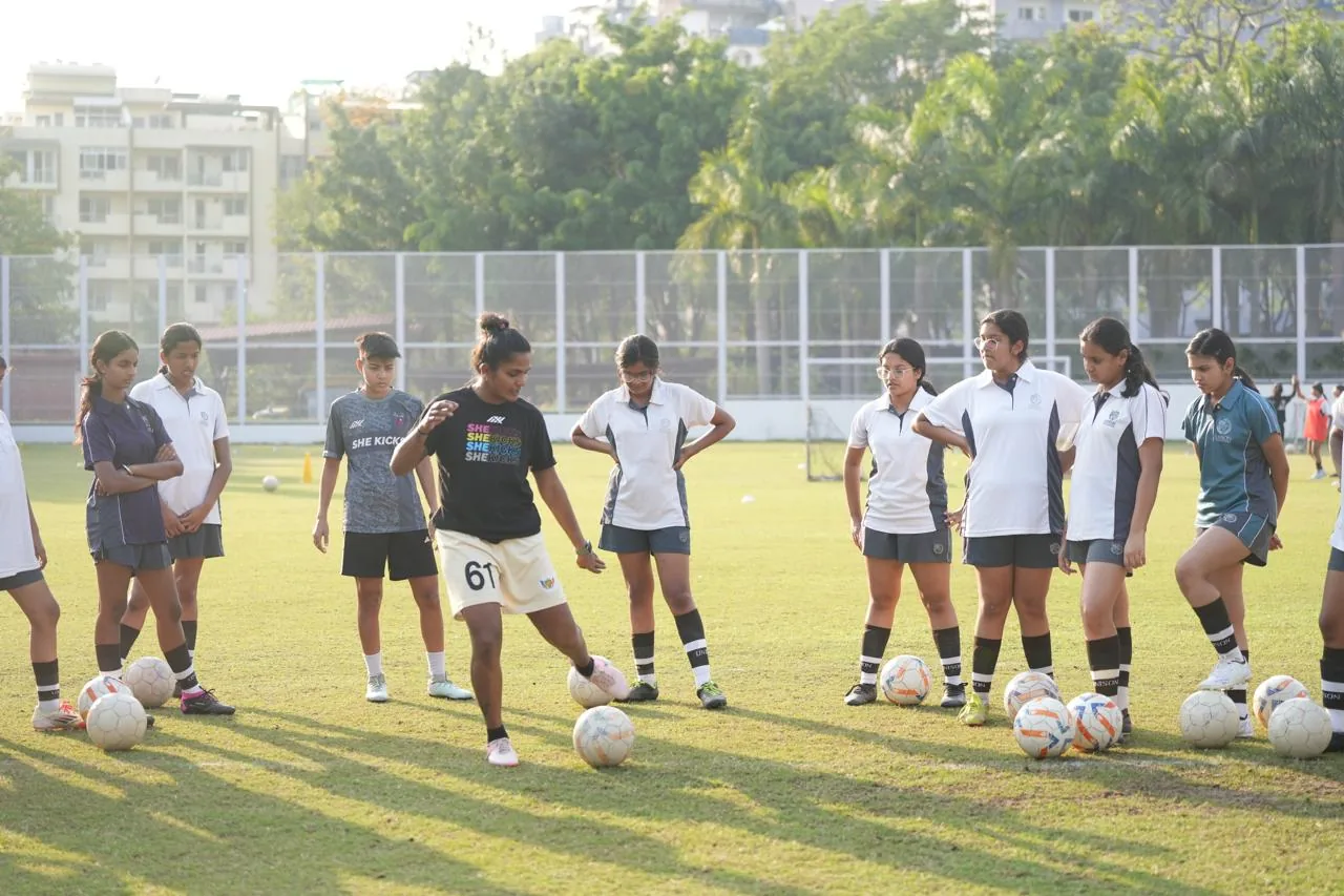 Aditi Chauhan demonstrating ball control to schoolgirls in white polos at a training session