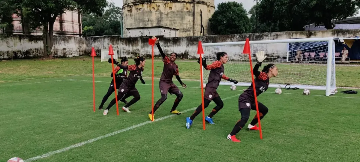 Goalkeepers running agility warm-up drills around marker poles in front of the goal.