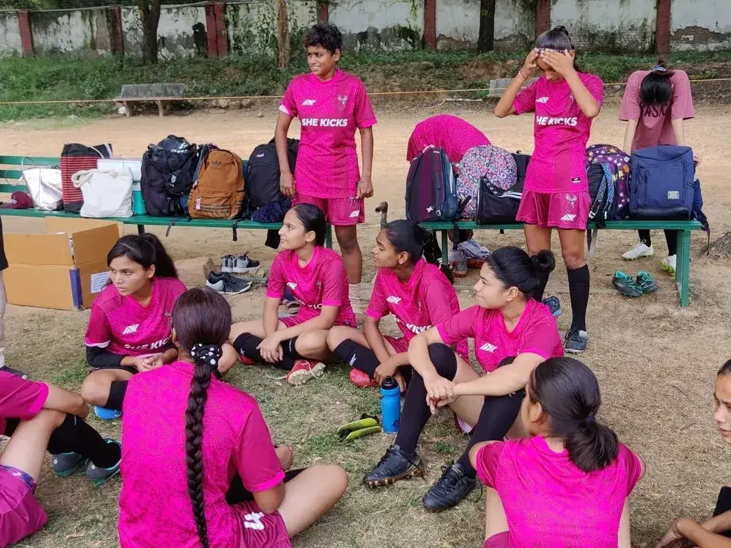 A mentor talking to a seated group of She Kicks players in pink kit