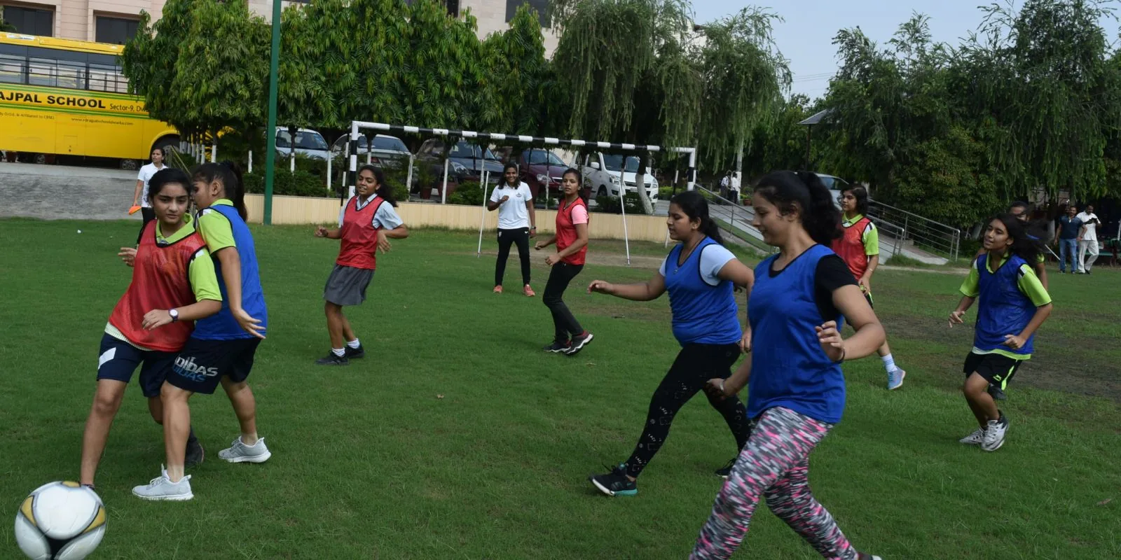Girls in coloured bibs playing a small-sided match on a school ground at a foundation session