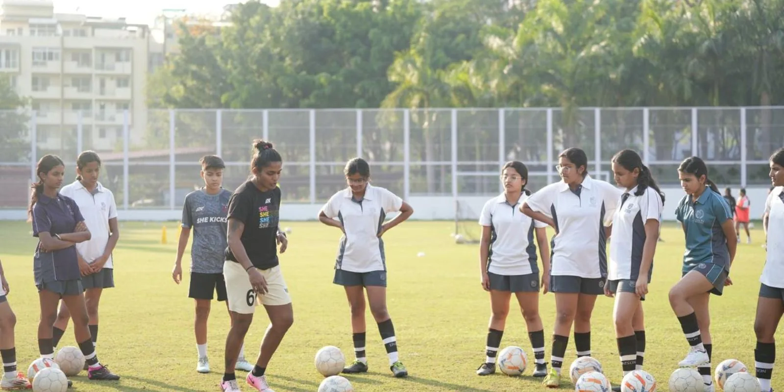 Aditi Chauhan demonstrating a skill to a line of schoolgirls with footballs at a training session