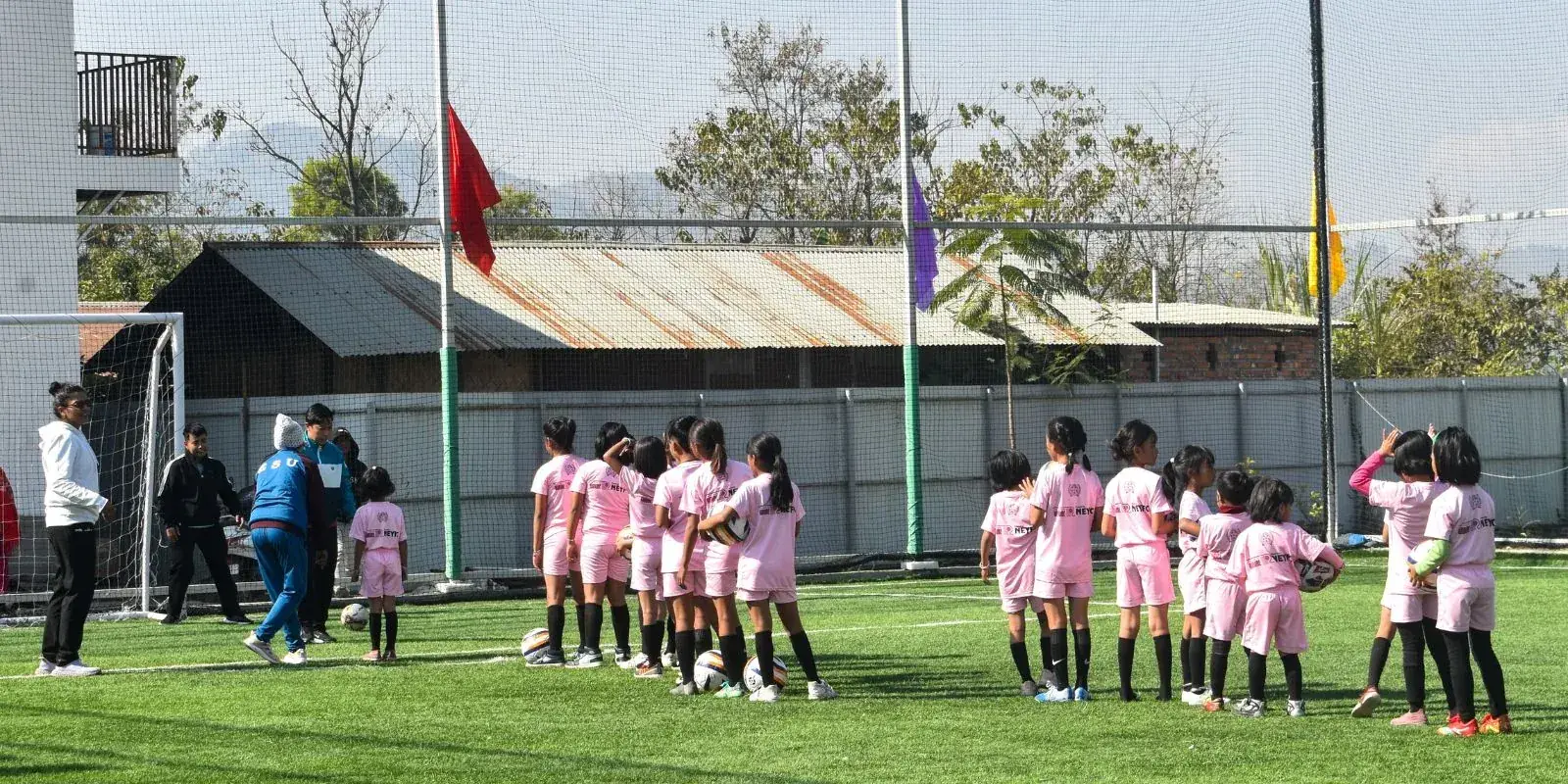 Young girls in pink kit lined up on a turf pitch in a hilly setting