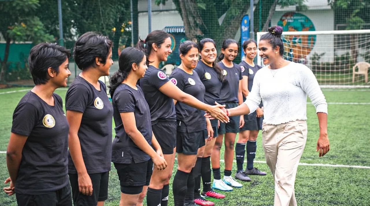 Aditi Chauhan greeting a line of She Kicks women's football players on a turf pitch