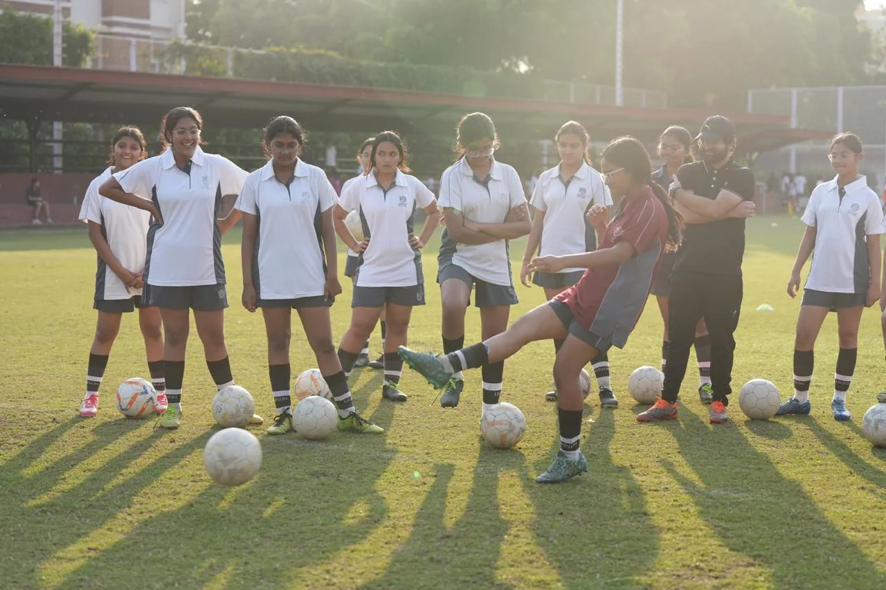 A girl striking a football as teammates look on during a She Kicks school training session