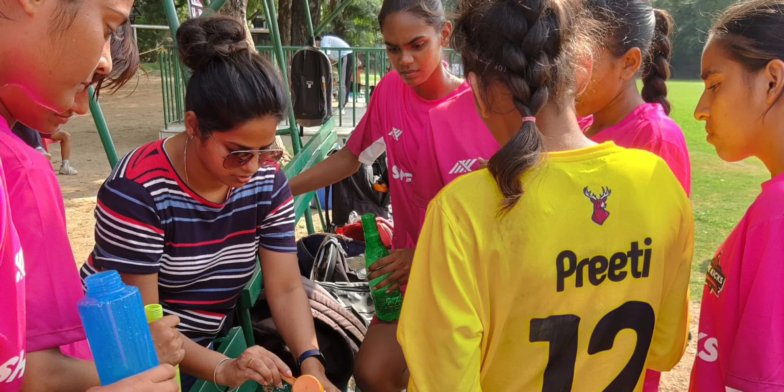A coach with girls in pink kit and a yellow-shirted goalkeeper at the sideline during a match