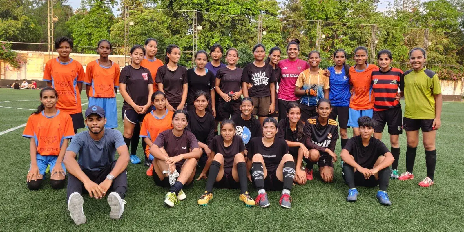 A large girls' football squad posing together for a team photo on a turf pitch