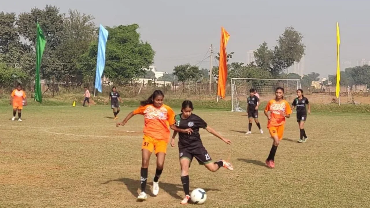 Players in orange and black kit chasing the ball in a She Kicks Football League match