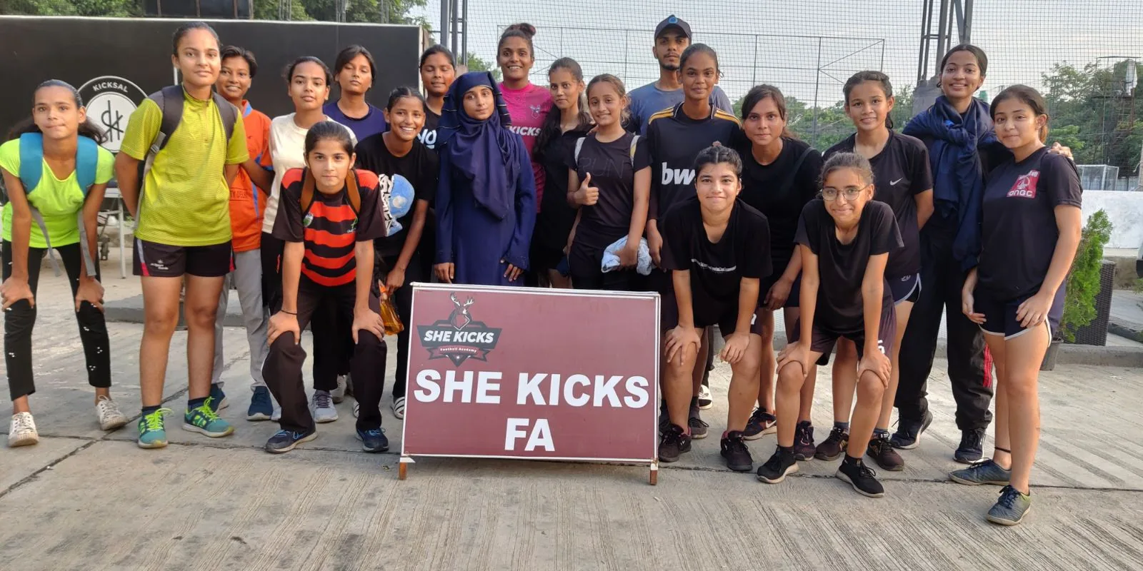 A large She Kicks FA girls' team posing for a group photo at a turf ground