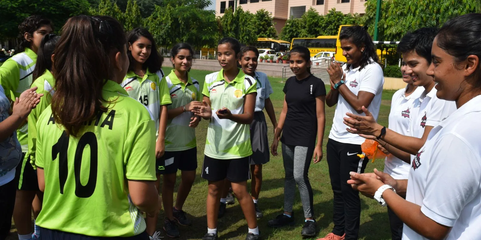 Aditi Chauhan and her team greeting a line of schoolgirls in green kit at a school ground