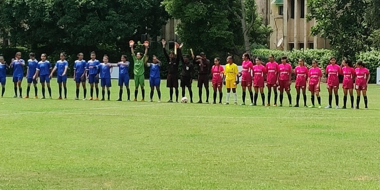 Two girls' teams in blue and pink kit lined up with match officials before a match