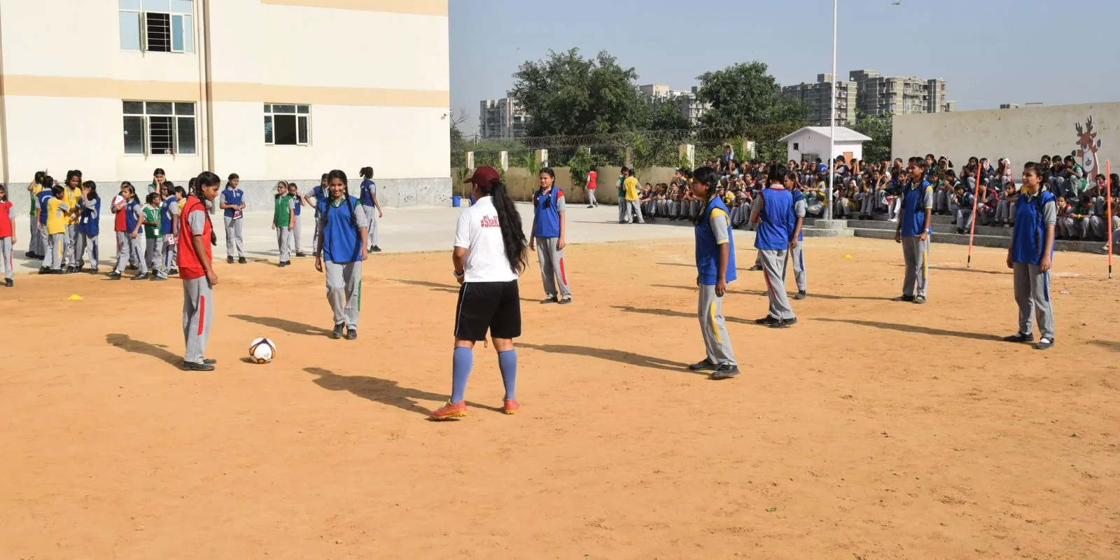A She Kicks coach refereeing girls in bibs as a crowd of seated schoolgirls watches